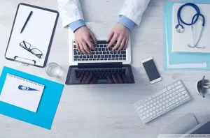 Un médico trabajando en una computadora portátil con un estetoscopio.
